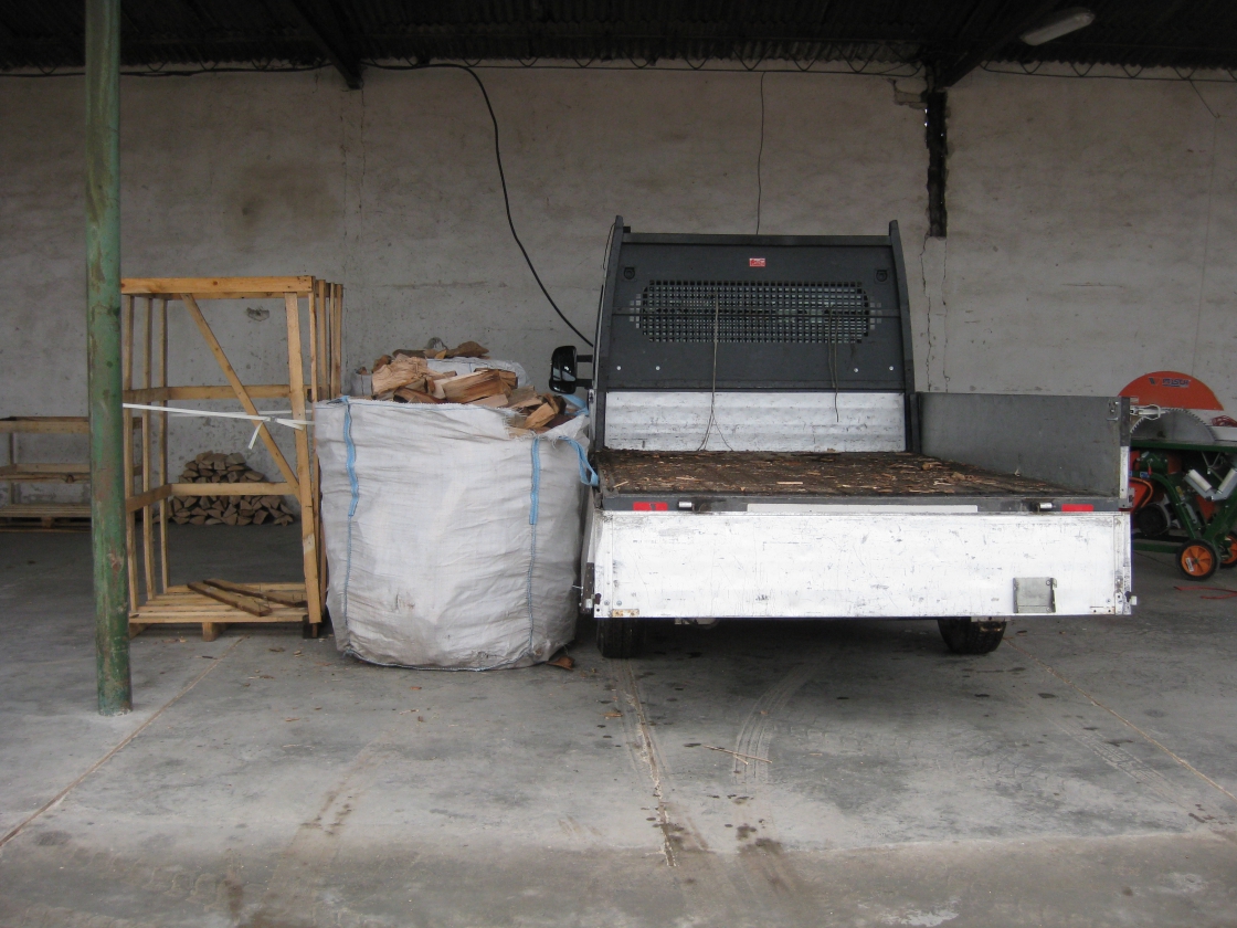 Une caisse en bois vide avec un sac plein de bois de chauffage à côté et une camionnette.