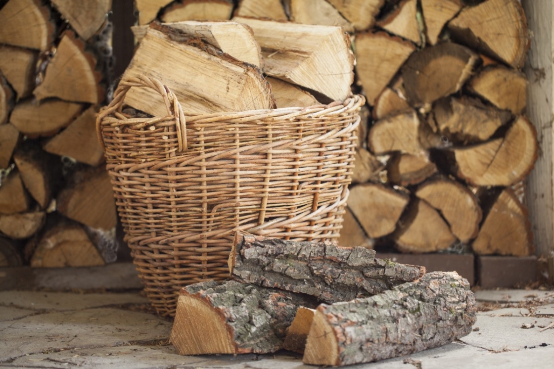 Een mand met brandhout met daarachter een opeenstapeling van brandhout.