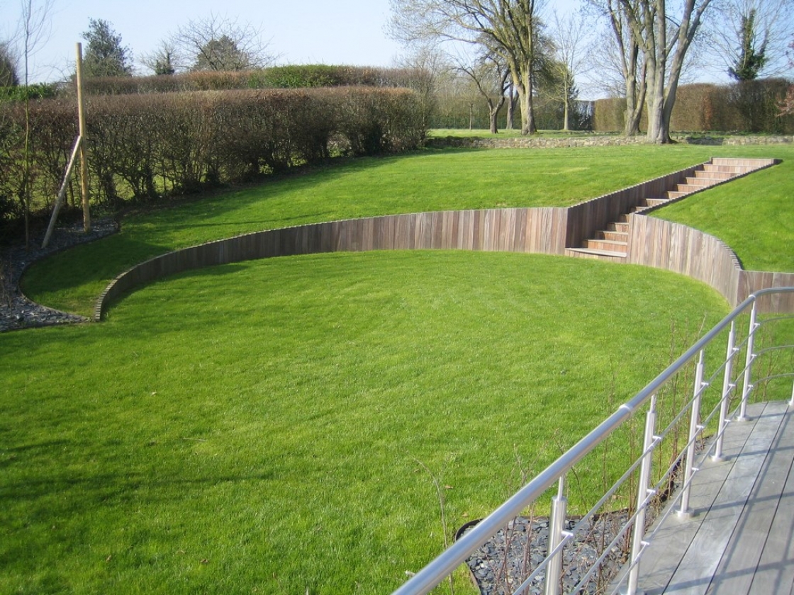 Een groot stuk groen gras met een gebogen houten keerwand.