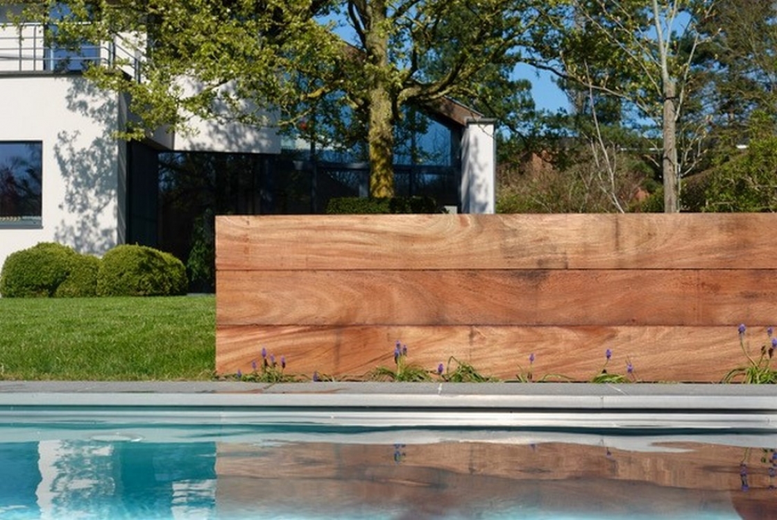 Een laag muurtje van tropisch hardhout bij een zwembad.