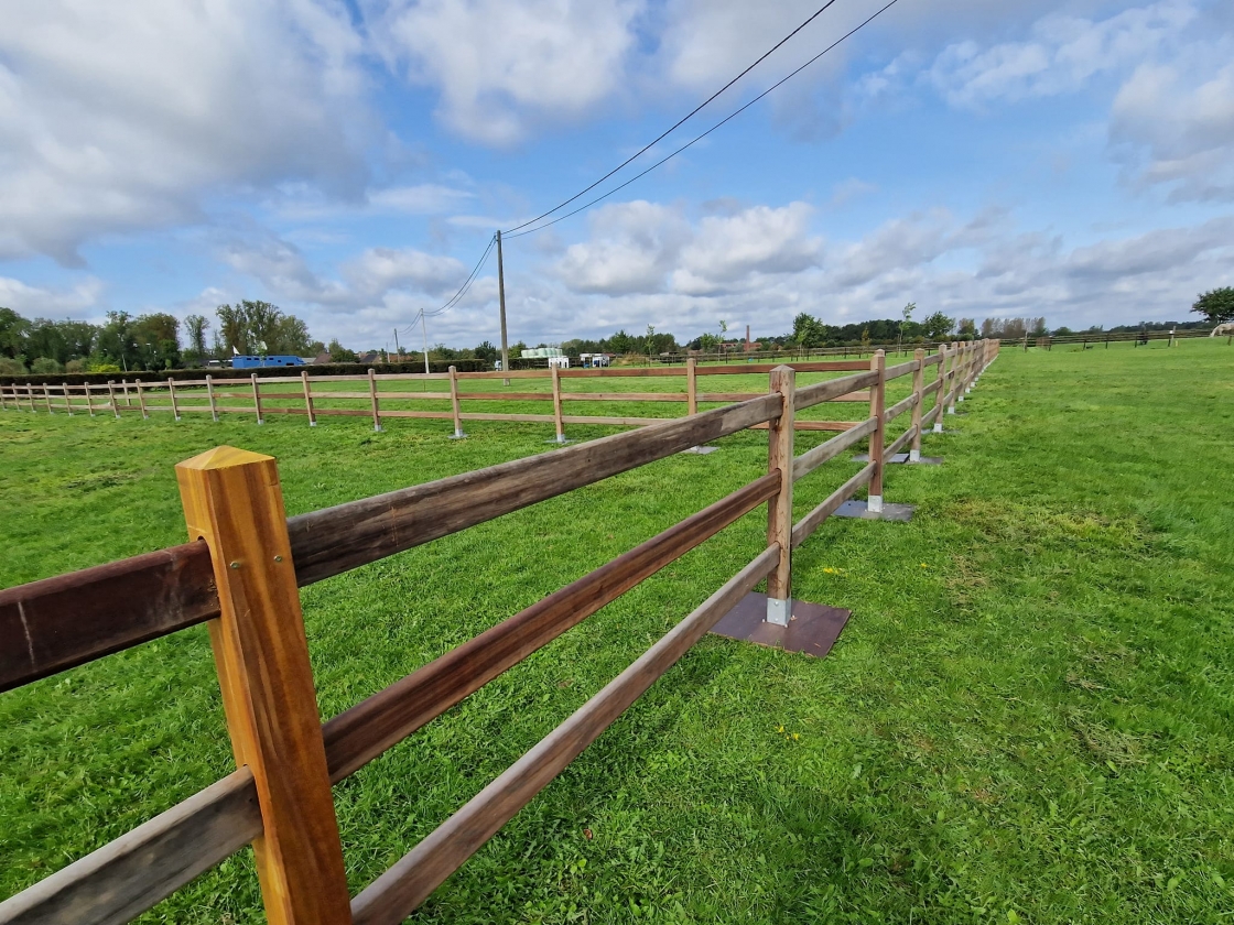 Een houten paardenomheining op een groene paardenweide.